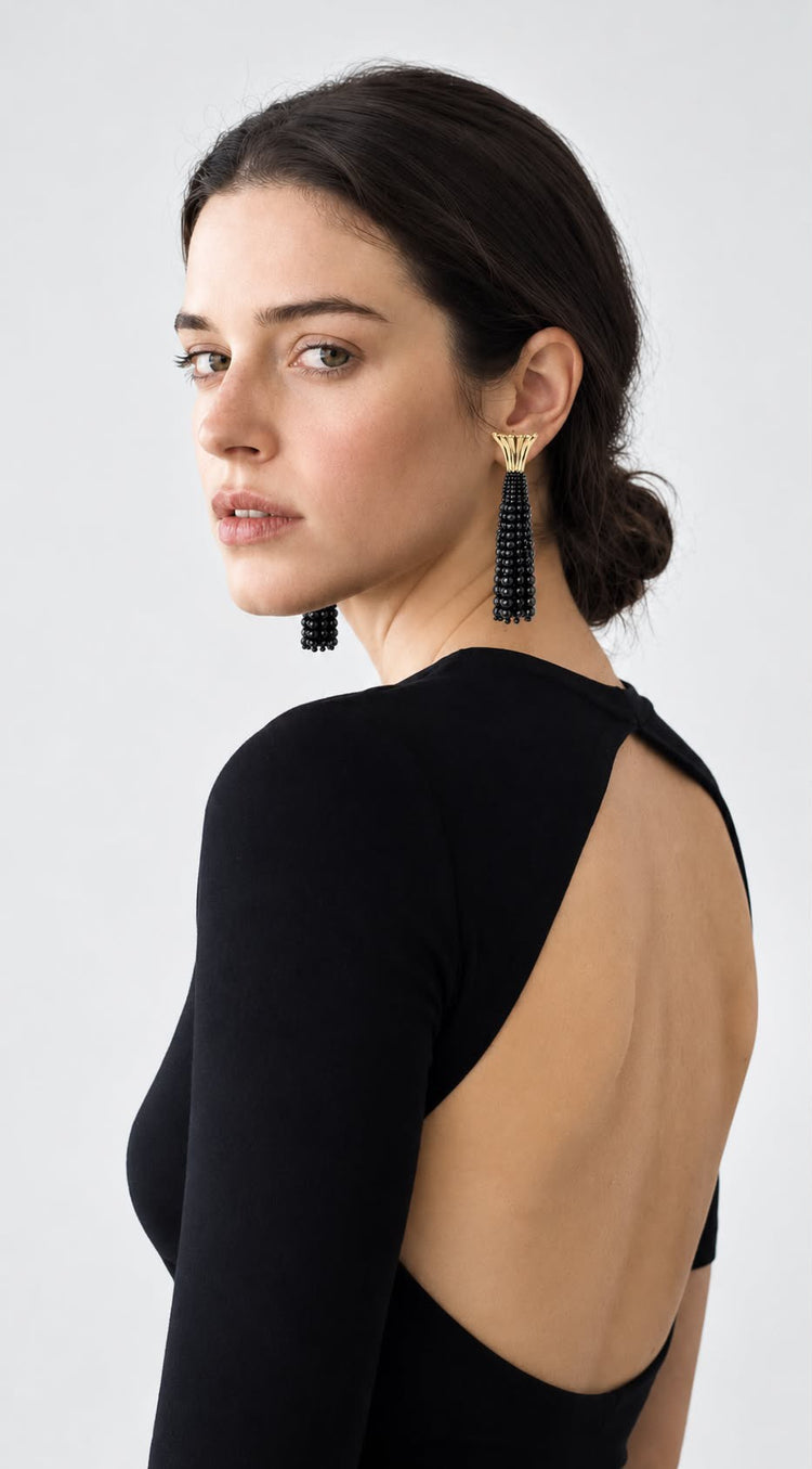 Model seen from behind in an open-back black top, wearing a black beaded tassel earring
