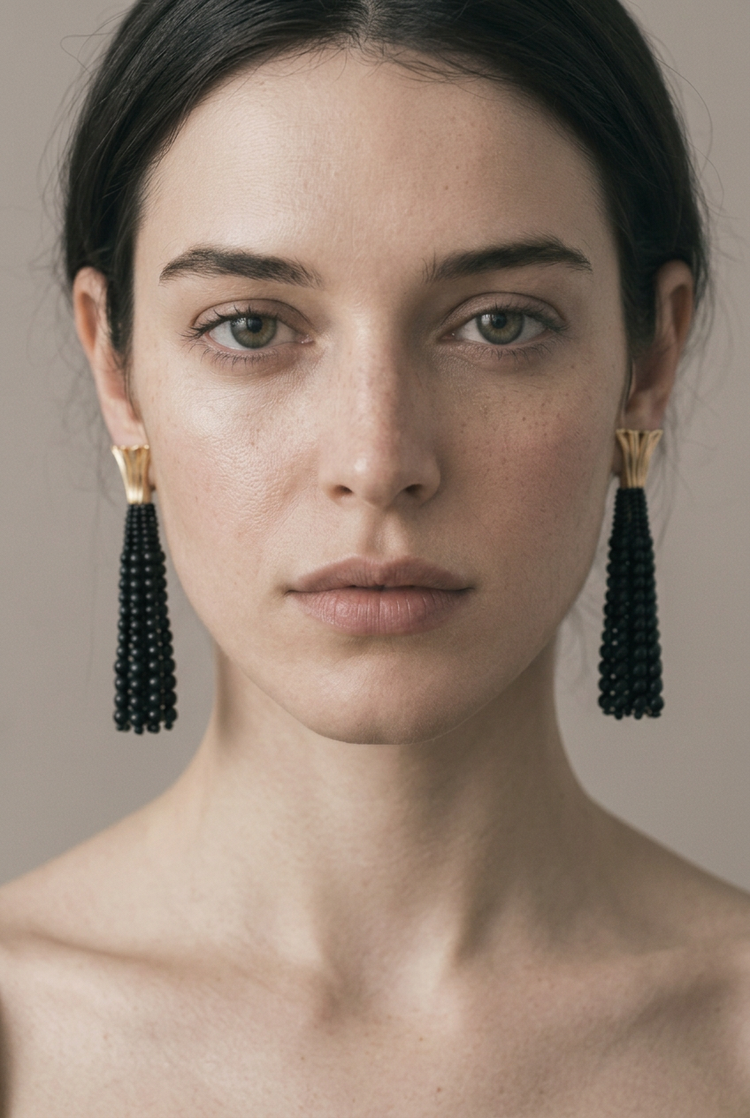 Close-up of the model facing the camera, wearing black beaded tassel earrings with gold fan tops