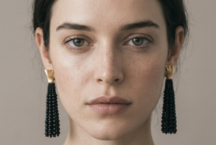 Close-up of the model facing the camera, wearing black beaded tassel earrings with gold fan tops